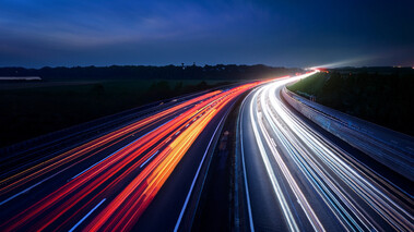 Langzeitbelichtung einer Autobahn bei Nacht mit bunten Lichtspuren.